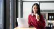 © wichayada - Smiling young Asian businesswoman holding a coffee mug and laptop at the office. Looking at the camera.