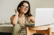 © Ilona - Young smiling female student using a laptop and headphones is watching an online lesson.