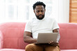 © amorn - African American male working with laptop computer on sofa at home