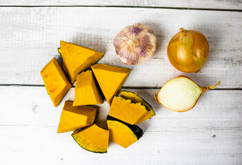 Pumpkin or Jerimum cut into pieces on a wooden background with garlic and onion. From the family Cucurbitaceae and genera Abobra and Cucurbita rich in vitamins and very used to make sweets and purees.