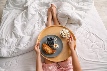 Woman holding wooden tray with tasty breakfast on bed