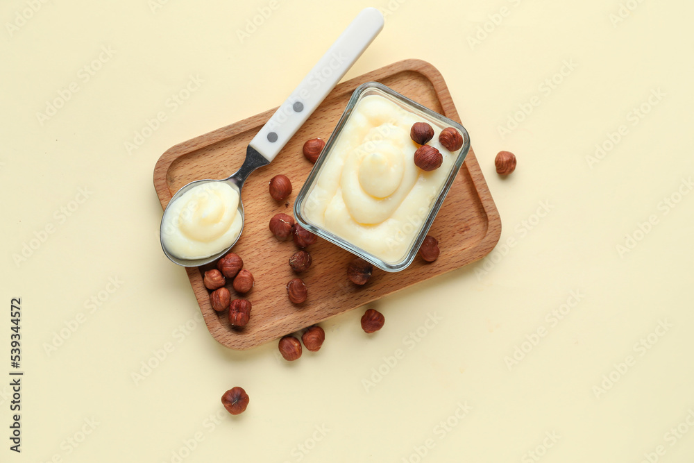 Wooden board with tasty vanilla pudding and hazelnuts on color background