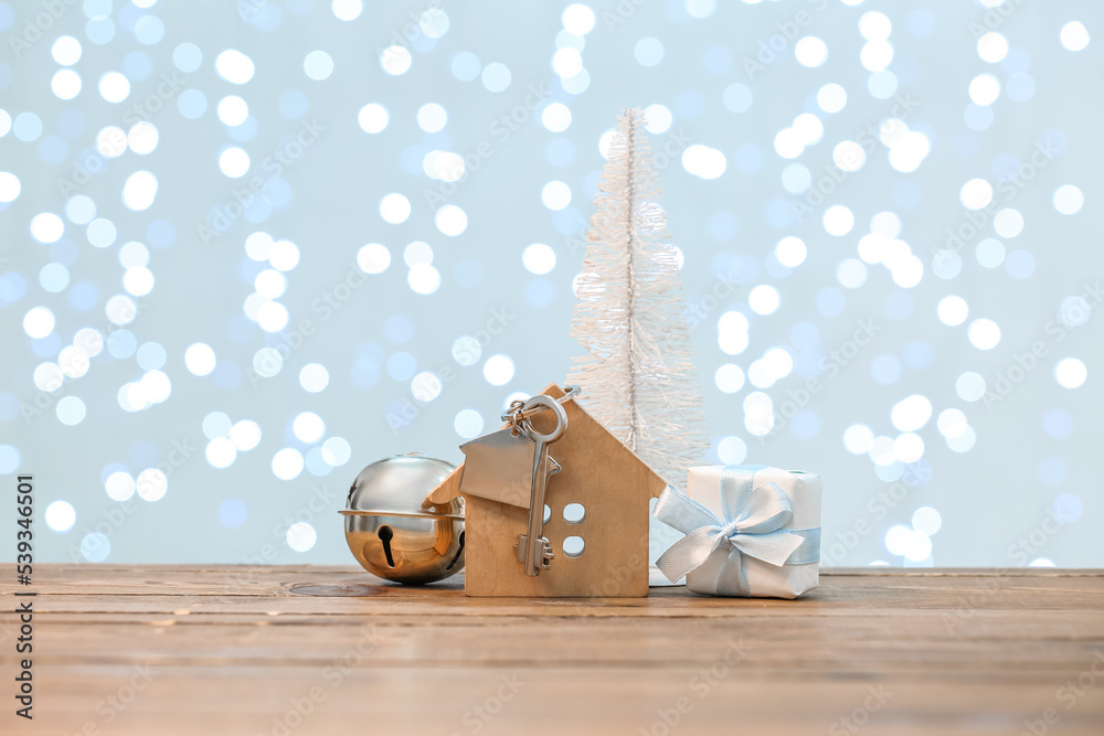 House figure with key, Christmas tree, bell and gift on table against blurred lights