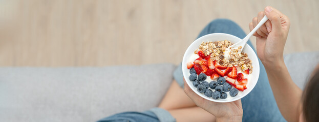 Woman having delicious healthy breakfast at home on morning. Health care female eats yogurt with granola and berry fruit. Healthy food, Vitamins, clean diet, dieting, detox, vegetarian, organic food.