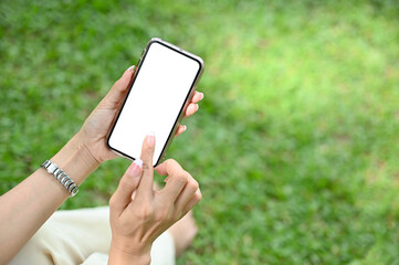 Close-up, A female relaxing in the park, sitting on grass and using her smartphone.