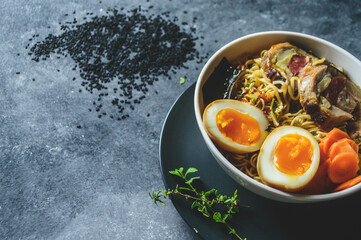 Sopa ramen Japonés, porchetta y huevo en tazón blanco, sobre un plato negro en un fondo oscuro