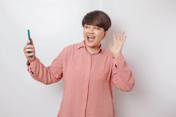 A portrait of a happy Asian woman is smiling and holding her smartphone wearing a pink shirt isolated by a white background