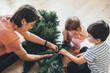 © Strelciuc - Close-up view of happy loving young caucasian mother and two little kids having fun assembling Christmas tree together. Celebrate New Year holidays. Eco