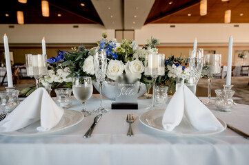 Sweetheart sign on table in ballroom with blue and white wedding floral centerpiece on white table cloth surrounded by place settings and glassware. blue hydrangeas white roses horizontal no people