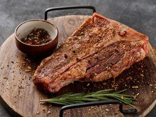 Wall Mural - Raw fresh meat T-bone steak, seasoning on chopping cutting wooden board on grey background.