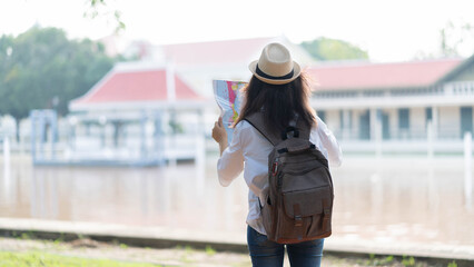 Wall Mural - Hipster tourist traveler with backpack and hat looking the map with temple Thailand background