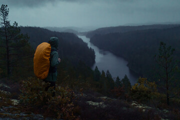 a man with a backpack standing on a rock in the forest looking over a river flowing in a forest on a