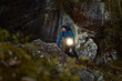 © Francis - Adventurous male hiker exploring a dark rocky cave at night, holding a bright flashlight and wearing a blue jacket and backpack. High-quality outdoor exploration and wilderness survival concept.