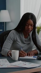 Poster - Vertical video: Black student drinking coffee while searching business information on internet using computer working at communication project. Focused woman sitting at desk in living room analyzing
