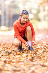 Young female athlete tying shoelaces before running in autumn park.