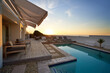 © Caia Image - Sunset over ocean behind modern, luxury patio swimming pool