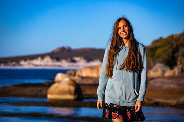 a beautiful long-haired woman in a skirt walks at sunset on the rocks by the ocean in western australia, a gorgeous beach with white sand and turquoise water in cape le grand national park near espera