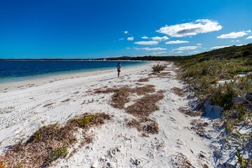 a long-haired girl in a dress walks on a paradise beach in western australia; a beach with turquoise water, white sand and massive mountains in the background