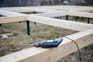 Close up view of drill laying on wooden pile foundation for future frame house. Constuction site and work instrument concept.