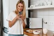 © Drobot Dean - Happy woman laughing and using cellphone while having breakfast at home
