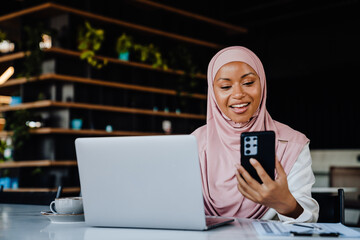 Wall Mural - Young muslim woman using cellphone working on laptop in office