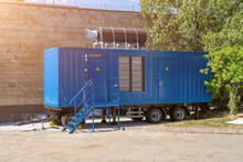 Modern Blue Diesel Powered Emergency Backup Electric Generator On Portable Trailer. Industrial Mobile Diesel Generator For Office Building, Connected To Electrical Network By Cable.
