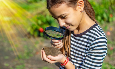 Wall Mural - Children examine the soil with a magnifying glass. Selective focus.