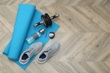 Poster - Exercise mat, ab roller, bottle of water, stopwatch and shoes on wooden floor, flat lay. Space for text