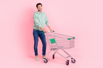 Poster - Full length photo of cheerful positive man wear trendy sweatshirt clothes hold cart go market isolated on pink color background