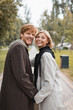 © LIGHTFIELD STUDIOS - positive blonde woman and cheerful redhead man holding hands while strolling in park.