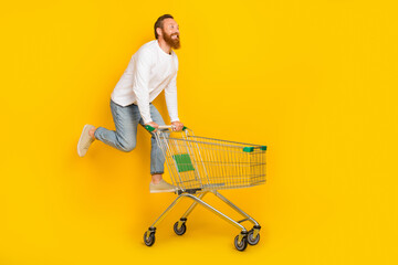 Wall Mural - Full size profile photo of beard man run trolley wear shirt jeans shoes isolated on yellow color background