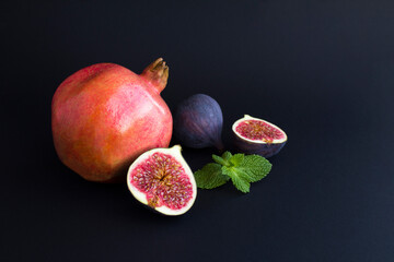 Wall Mural - Close-up on pomegranate and blue figs on the black background. Copy space.