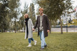 © LIGHTFIELD STUDIOS - full length of happy young man in coat holding hands with cheerful girlfriend while walking in autumnal park.