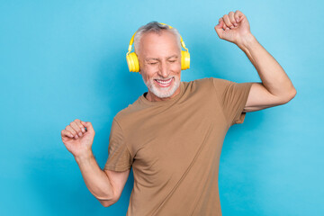 Canvas Print - Portrait of funky positive senior gray hair beard dressed beige t-shirt headphones dancing having fun isolated on blue color background