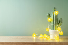 Christmas Holiday Greeting Card With Cactus As Alternative Christmas Tree And  Lights Garland On Wooden Shelf Over Green Background