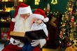 © ZaStock - Santa Clause reads a book to a little cute boy while sitting near Christmas tree. New Year concept