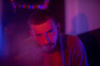© MartaKlos - A brutal man with a beard sits in a bar, smokes and exhales smoke. A guy looks at the camera in purple light.