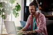 © lordn - Young cheerful man with a sleeve tattoo using laptop computer. Freelance entrepreneur working from home