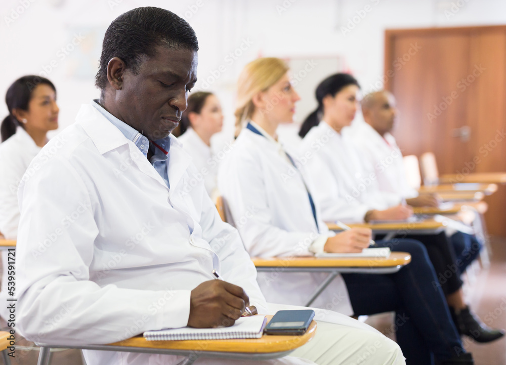 African american man in white lab coat taking notes during lecture at ...