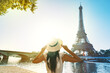 © Creative Cat Studio - Young woman tourist in sun hat and white dress standing in front of Eiffel Tower in Paris at sunset. Travel in France, tourism concept