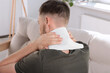 © New Africa - Man using heating pad at home, back view