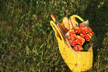 Sticker - Yellow wicker bag with beautiful roses, bottle of wine and baguettes on green grass outdoors. Space for text