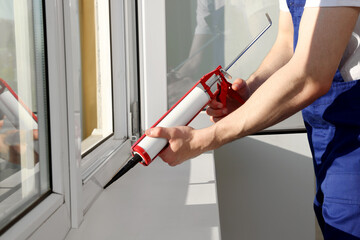 Wall Mural - Worker sealing plastic window with caulk indoors, closeup. Installation process