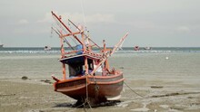 A Tilt Down Reveal Shot Of A Moored Beached Squid Fishing Boat During Low Tide In Thailand