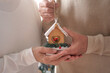 © luciano - Close-up view on the hands of a senior couple holding a little wooden house as decoration for Christmas tree.