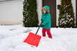 Child playing in snow with shovel. Girl shoveling fresh snow and clearing sidewalks near home after snowstorm. Kids removaling snow after heavy snowfall