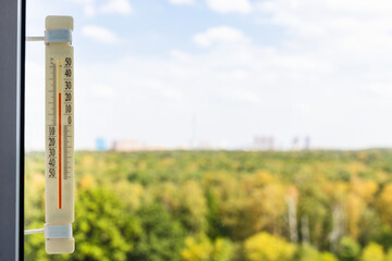 Wall Mural - thermometer on window pane on hot autumn day and green yellow trees of city park outside window (foc