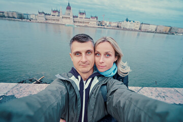 Wall Mural - Travel by Hungary. Pretty young loving couple taking selfie together against Budapest Parlament building.