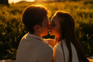 Wall Mural - close-up silhouette view of loving young couple sitting hugging and kissing on beautiful meadow with