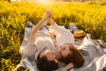 Wall Mural - happy smiling young couple in love lying holding hands and talking in field on sunny summer day, enj